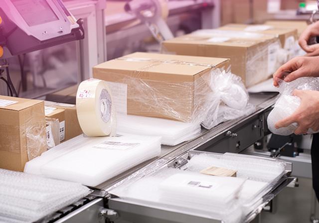 Línea de embalaje con cajas, cintas y estaciones de revisión final en una nave industrial bien iluminada